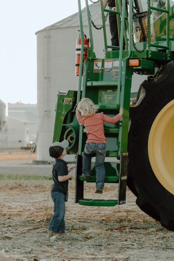 Two children climbing a tractor beside grain bins
